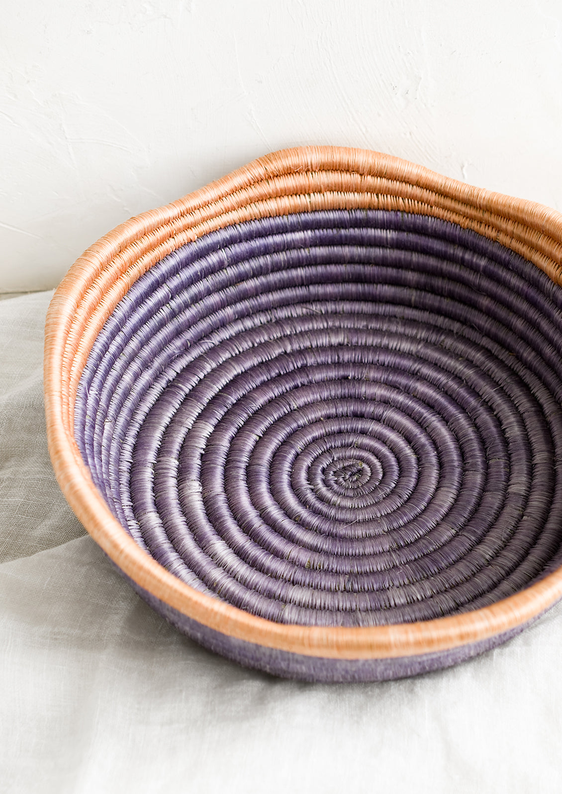 A purple woven shallow, round bowl with wavy peach rim at top.