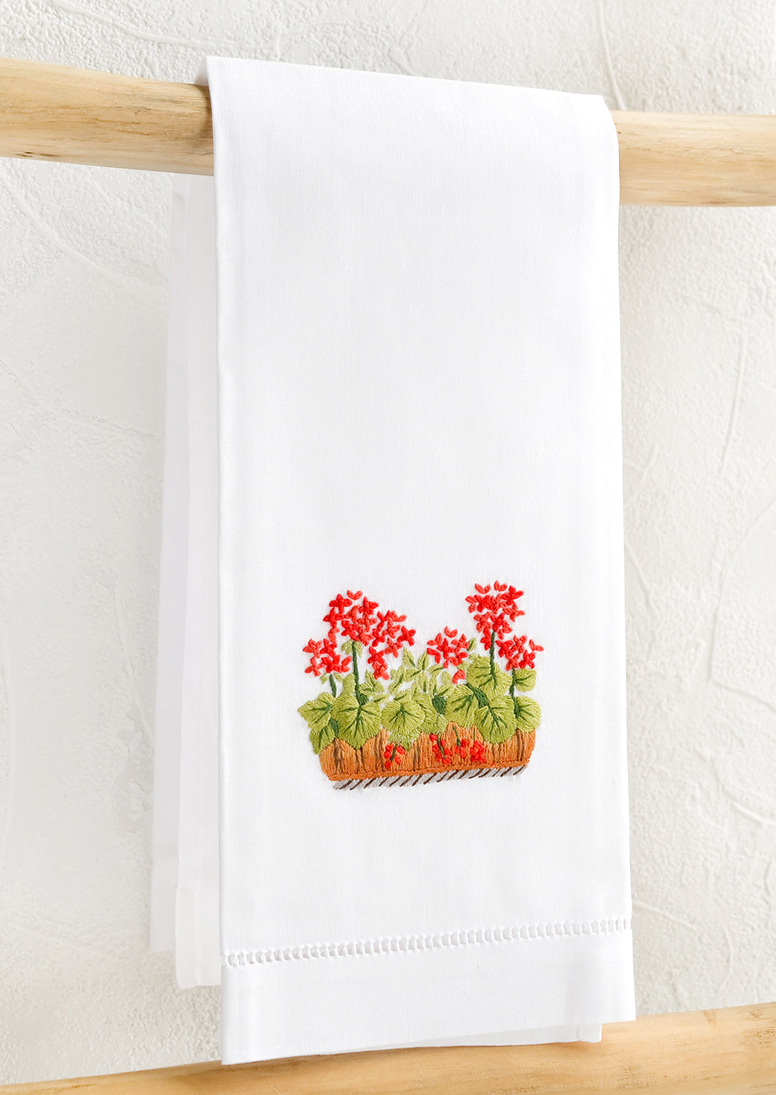 A white folded cotton hand towel with embroidered geranium design.