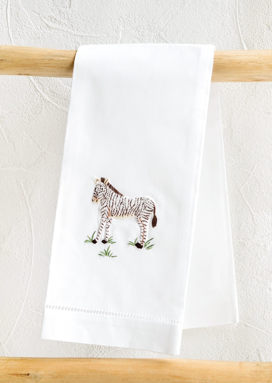 A white folded cotton hand towel with embroidered zebra design.
