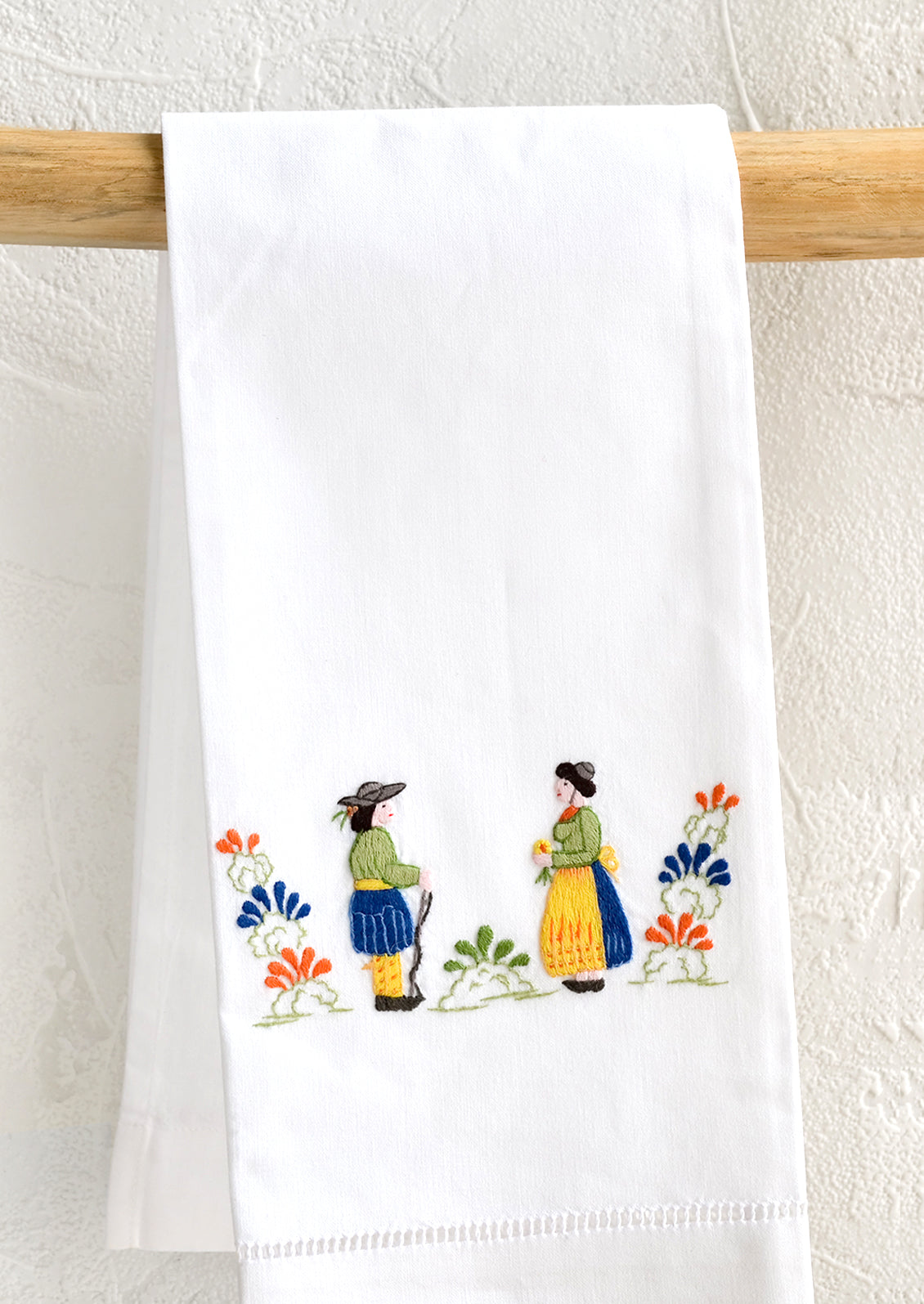 A white folded cotton hand towel with embroidered folk design.