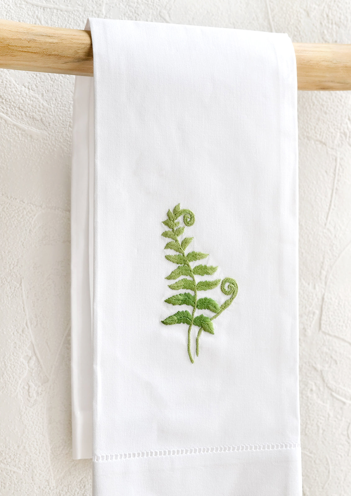 A white folded cotton hand towel with embroidered fern design.