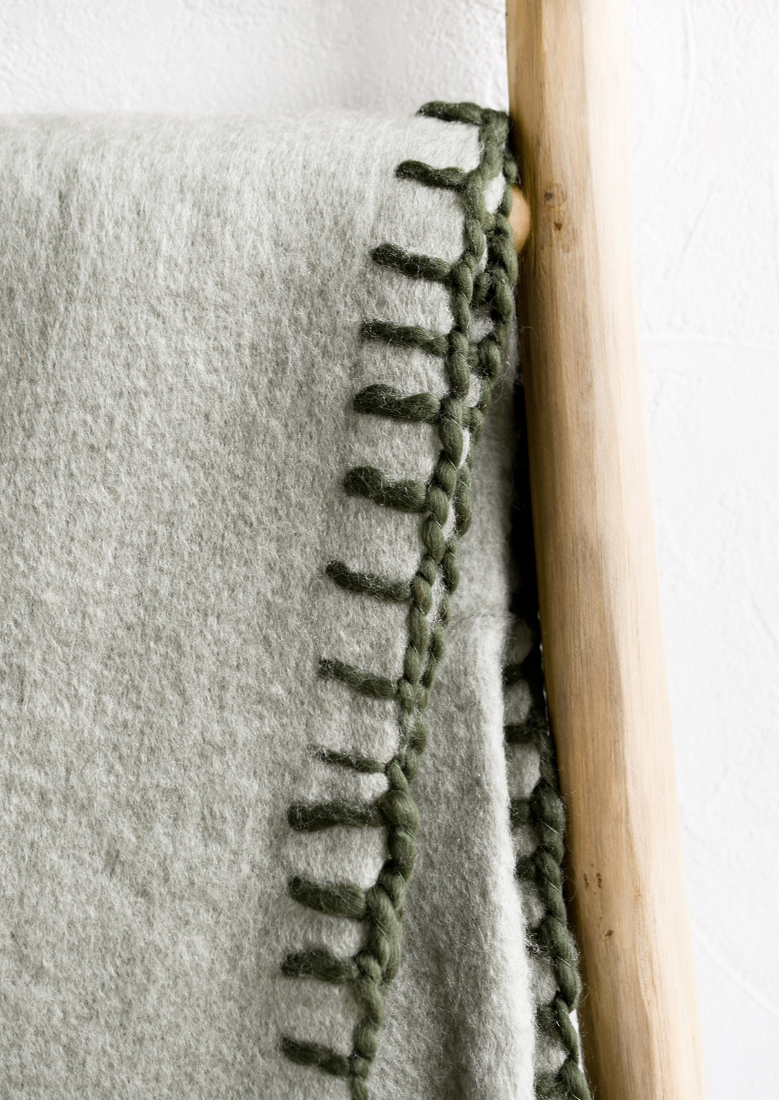 Yarn whipstitched finishing trim on a sage green blanket.