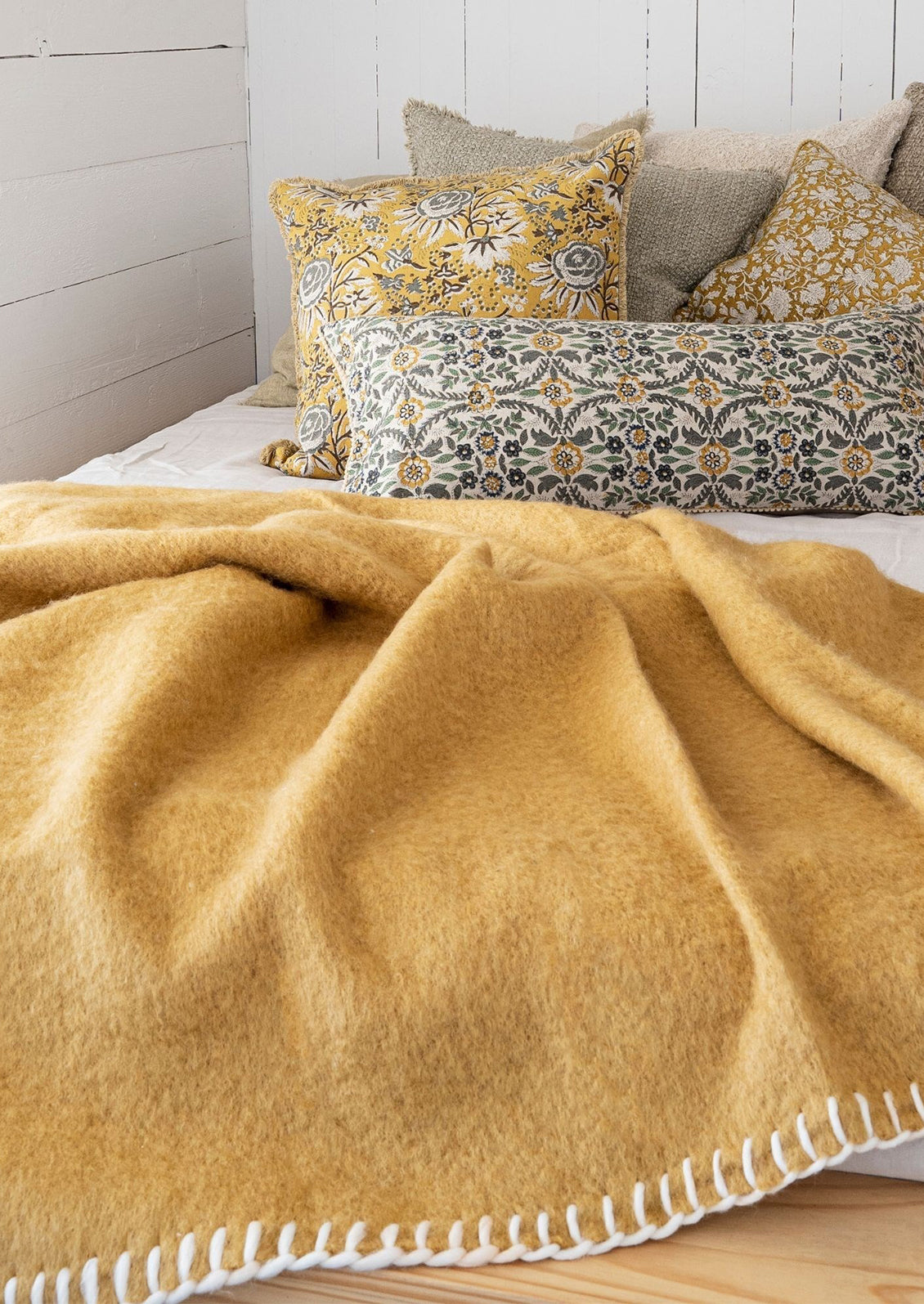 A mustard throw on a bed with throw pillows.