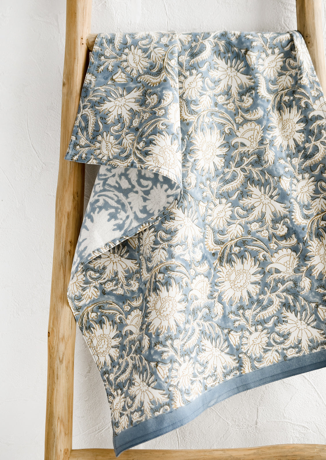 A block printed tea towel with floral pattern in blue, white and tan.