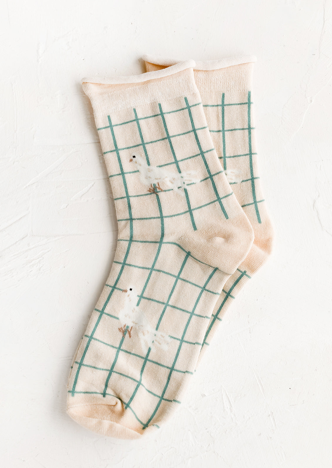 A pair of cream socks with aqua grid pattern and white bird graphic.