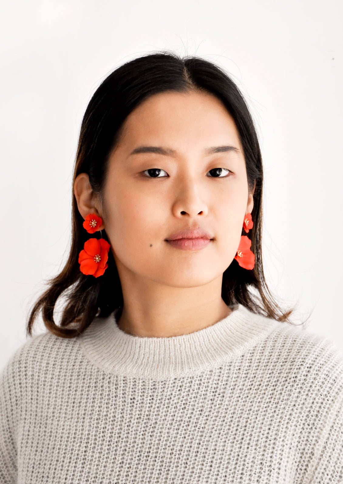 Model wears poppy red flower earrings and gray sweater.