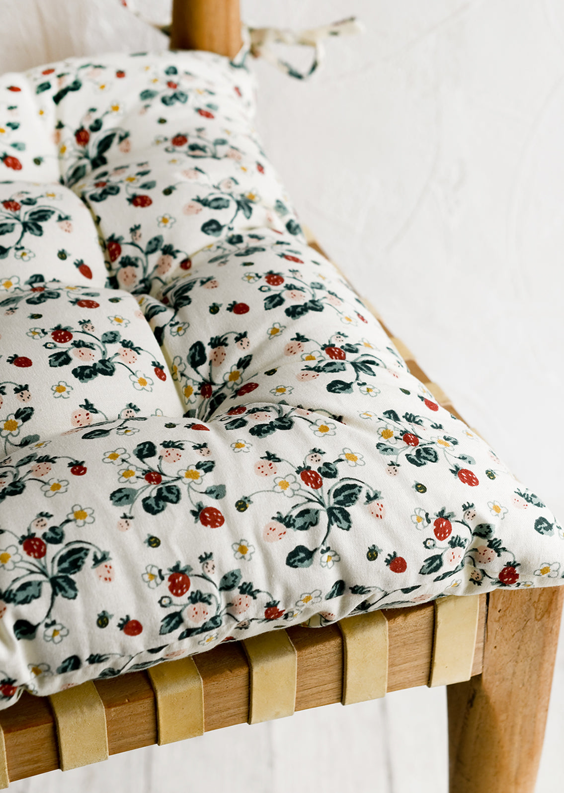 A square, quilted strawberry print chair cushion with corner ties.