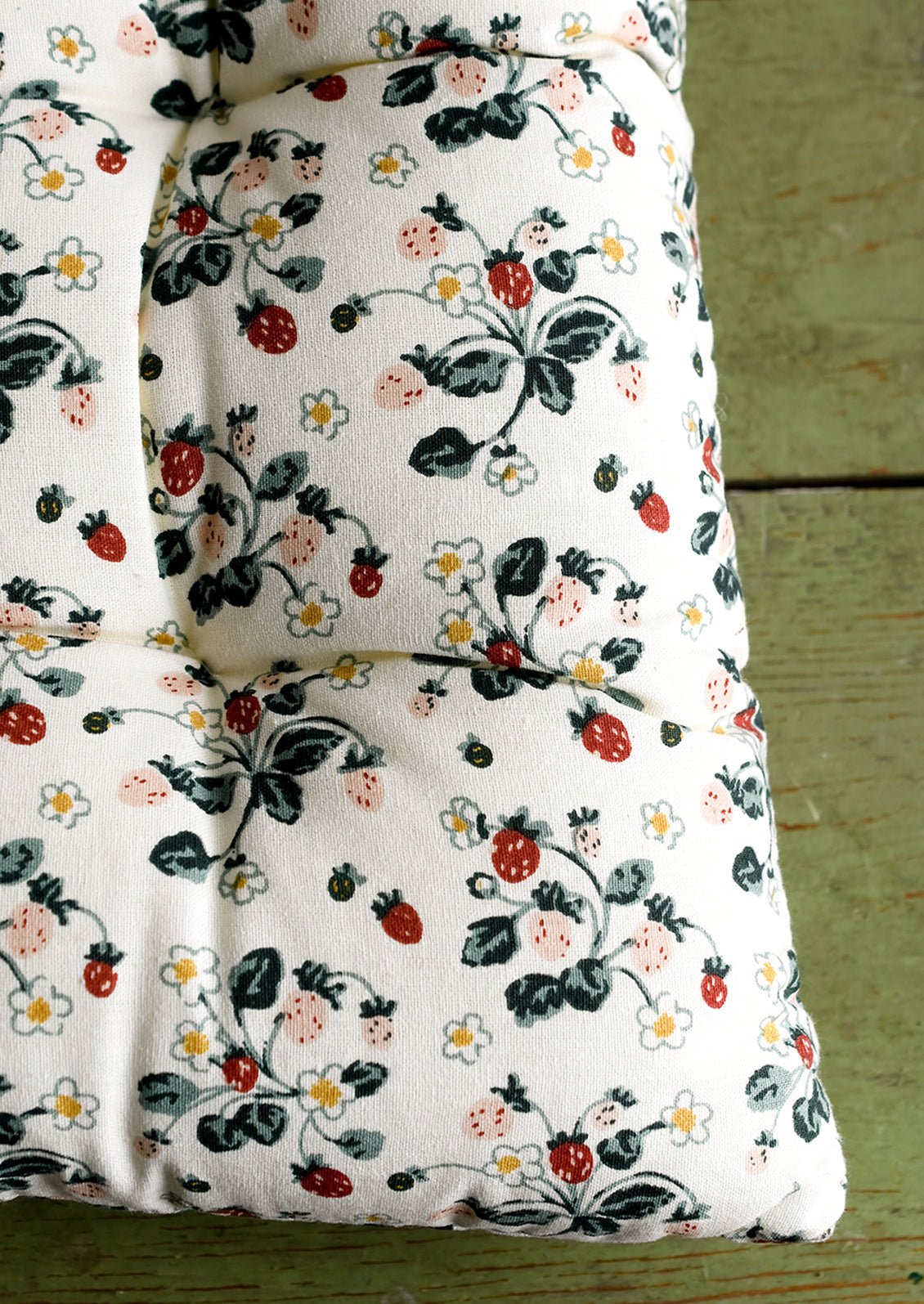A square, quilted strawberry print chair cushion with corner ties.