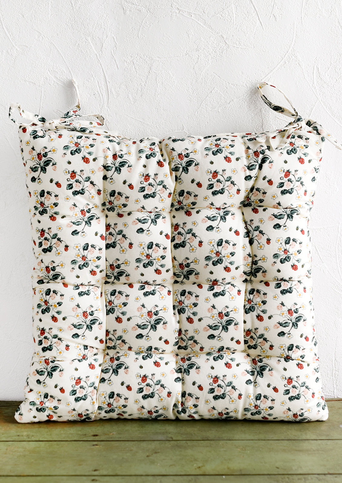 A square, quilted strawberry print chair cushion with corner ties.