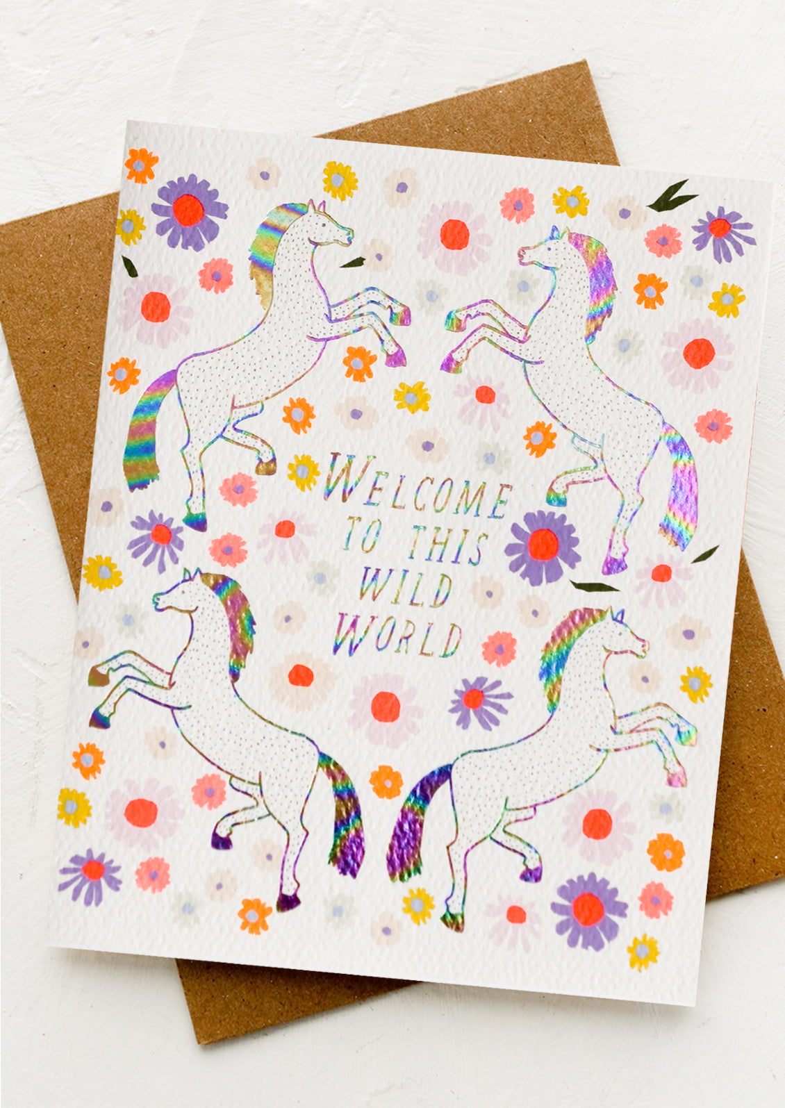 A greeting card with unicorn floral print, text reads "Welcome to this wild world".