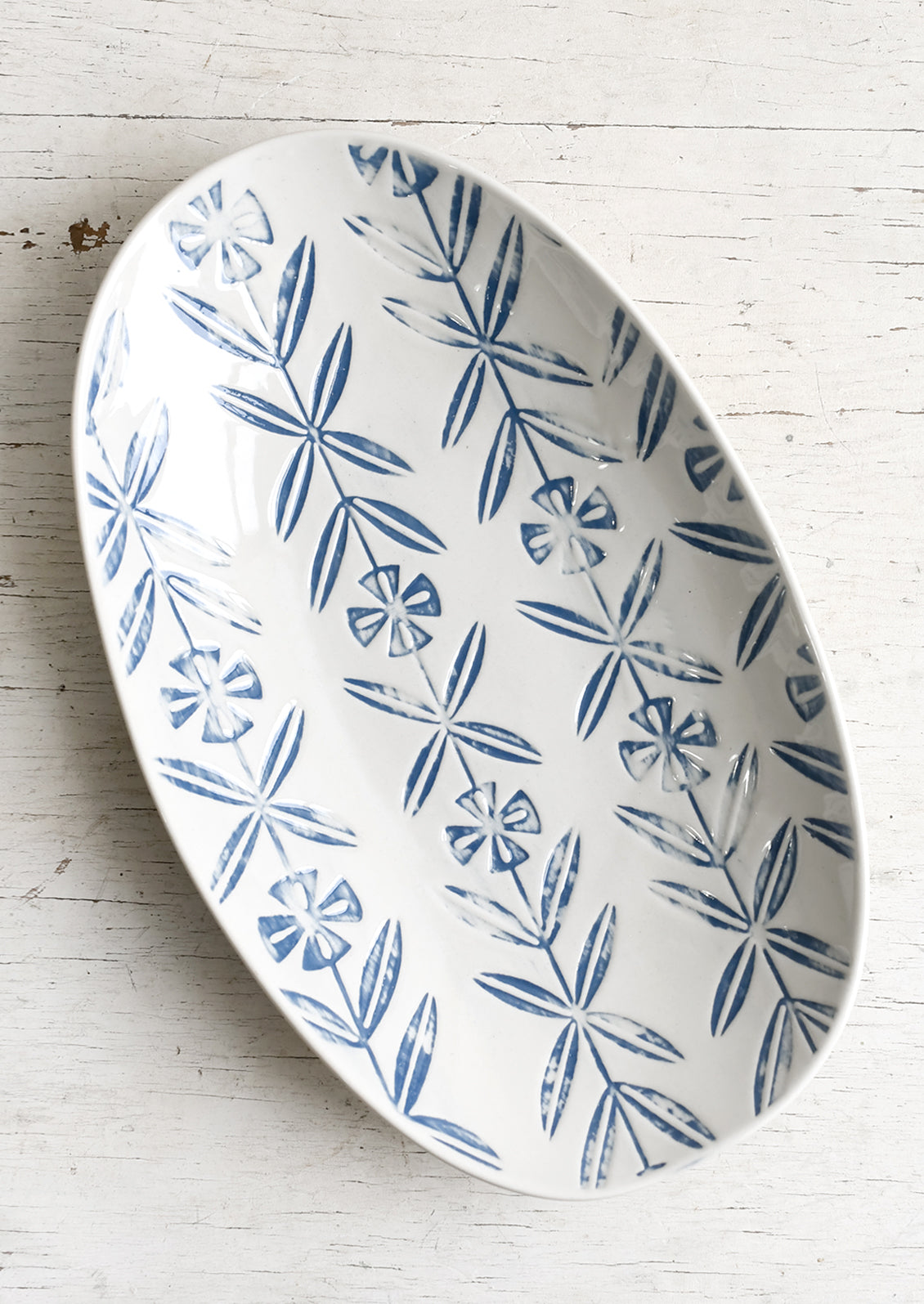 An oval shaped ceramic platter with blue imprint design.