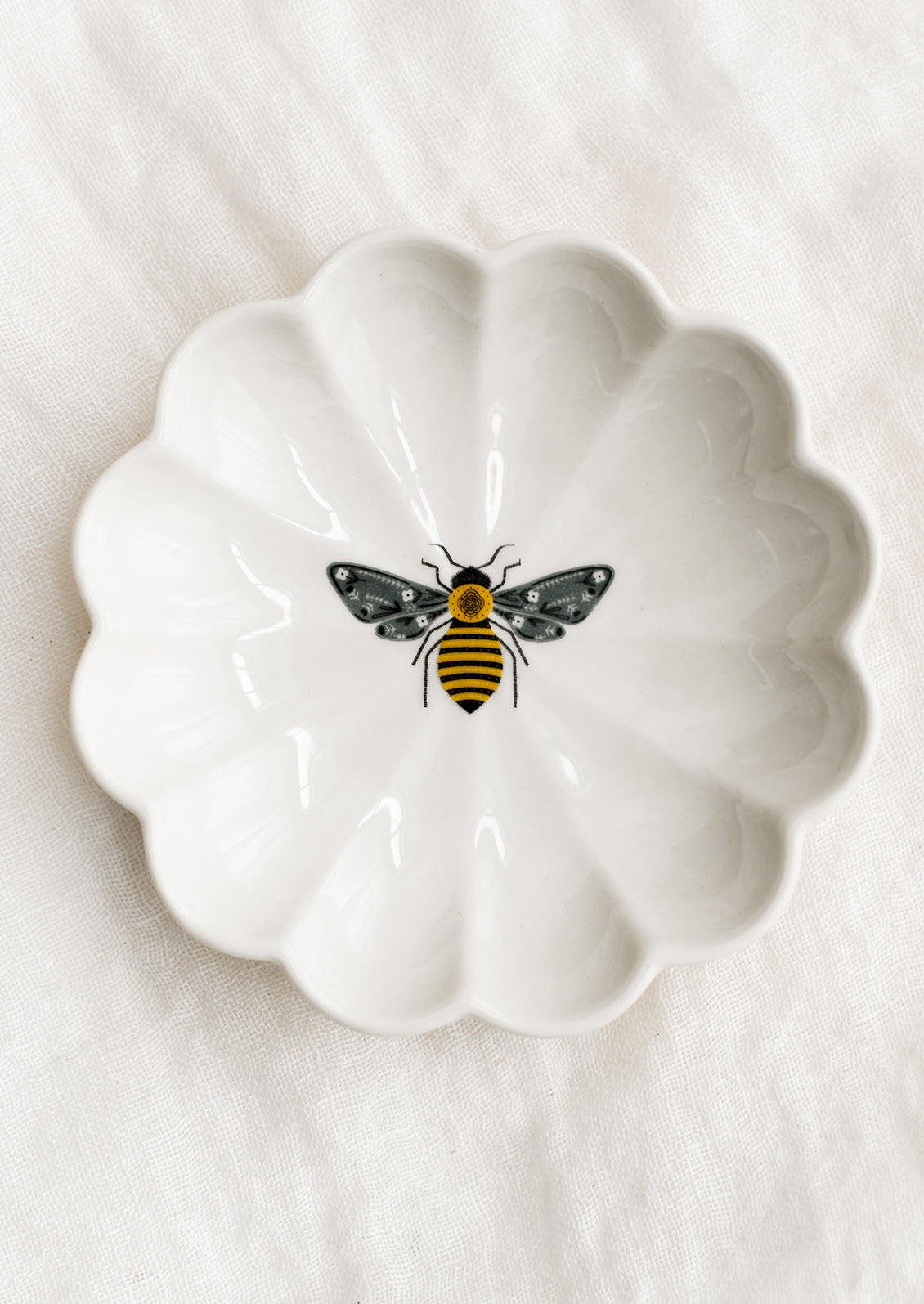 A white ceramic dish with scalloped shape and bee illustration at center.