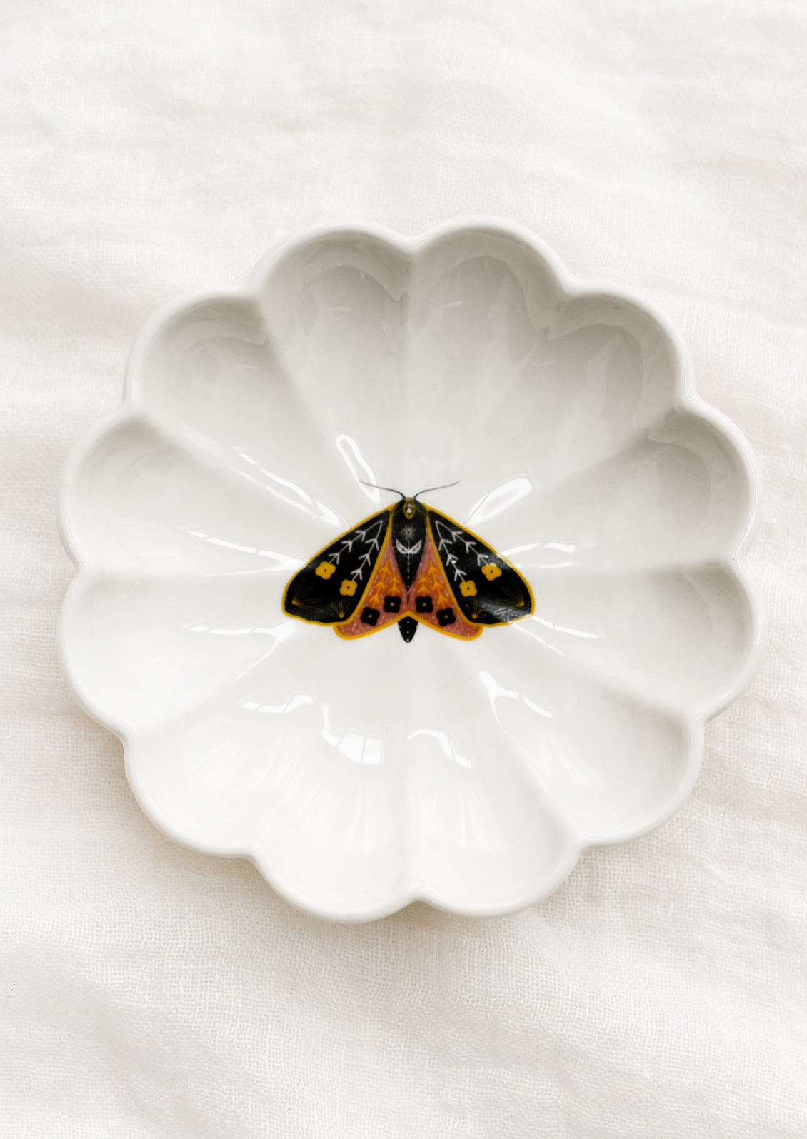 A white ceramic dish with scalloped shape and black and yellow moth illustration at center.