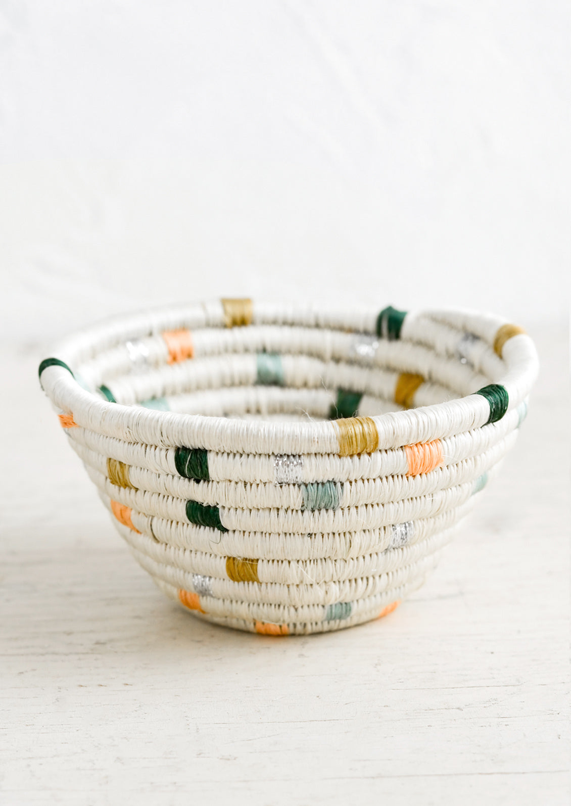 A small woven catchall bowl made from sweetgrass in white with pastel dashes.