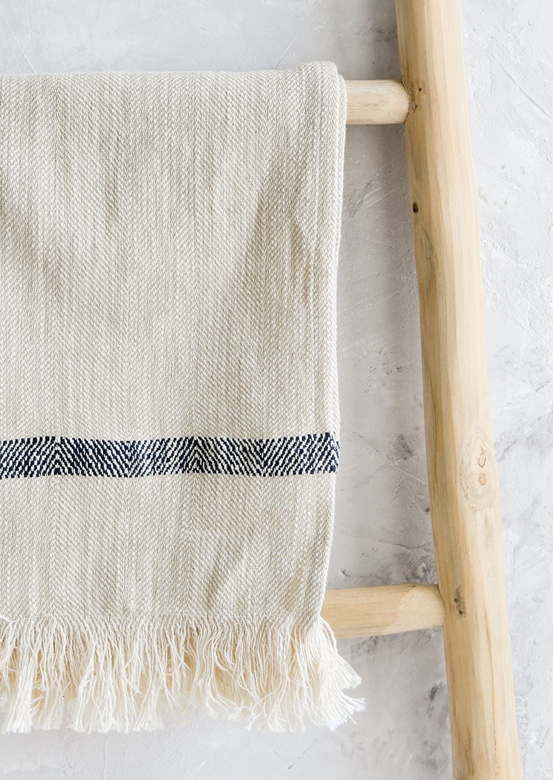 A woven kitchen towel with black stripe hanging on a ladder.
