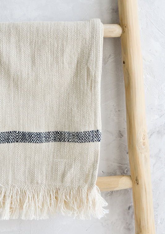 A woven kitchen towel with black stripe hanging on a ladder.