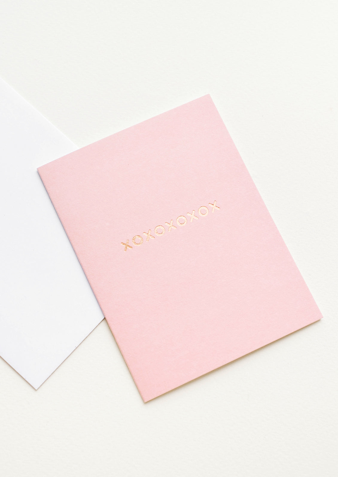 A white envelope and pale pink greeting card with "xoxoxoxoxox" in gold foil.