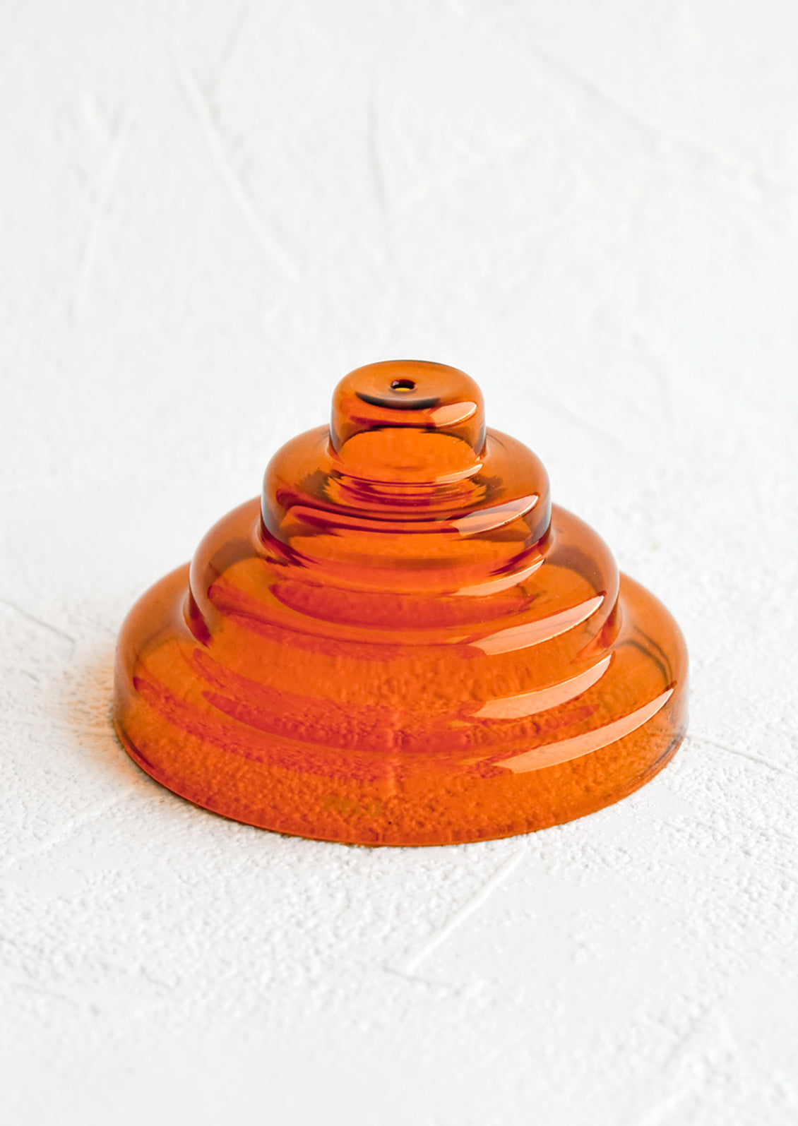 An incense holder made of glass in sculptural design with small hole at top, in amber.