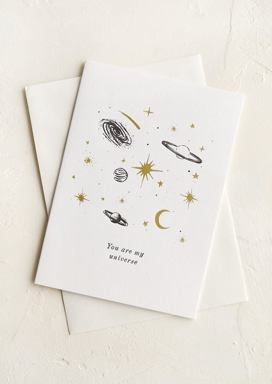 A greeting card with black and gold planets and text reading "You are my universe".