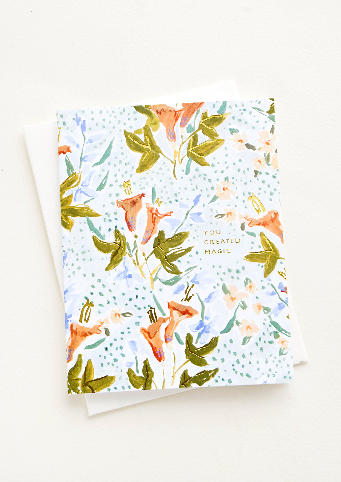Greeting card with floral illustrated background and small gold lettering reading "You Created Magic"