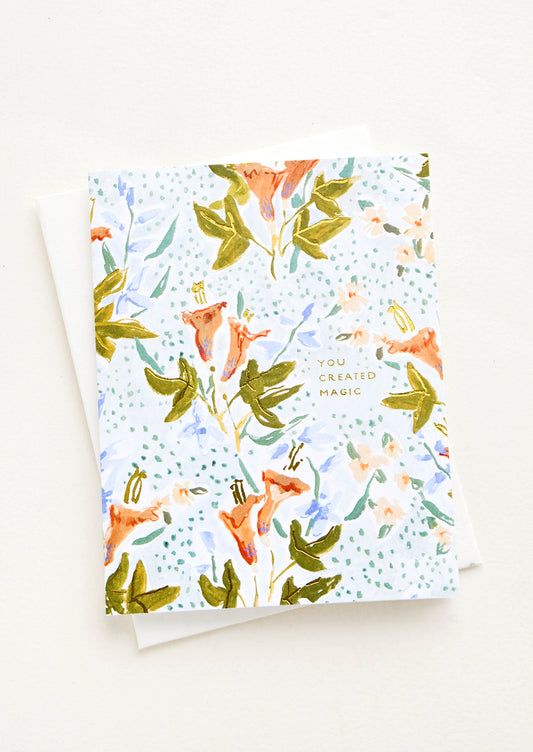Greeting card with floral illustrated background and small gold lettering reading "You Created Magic"