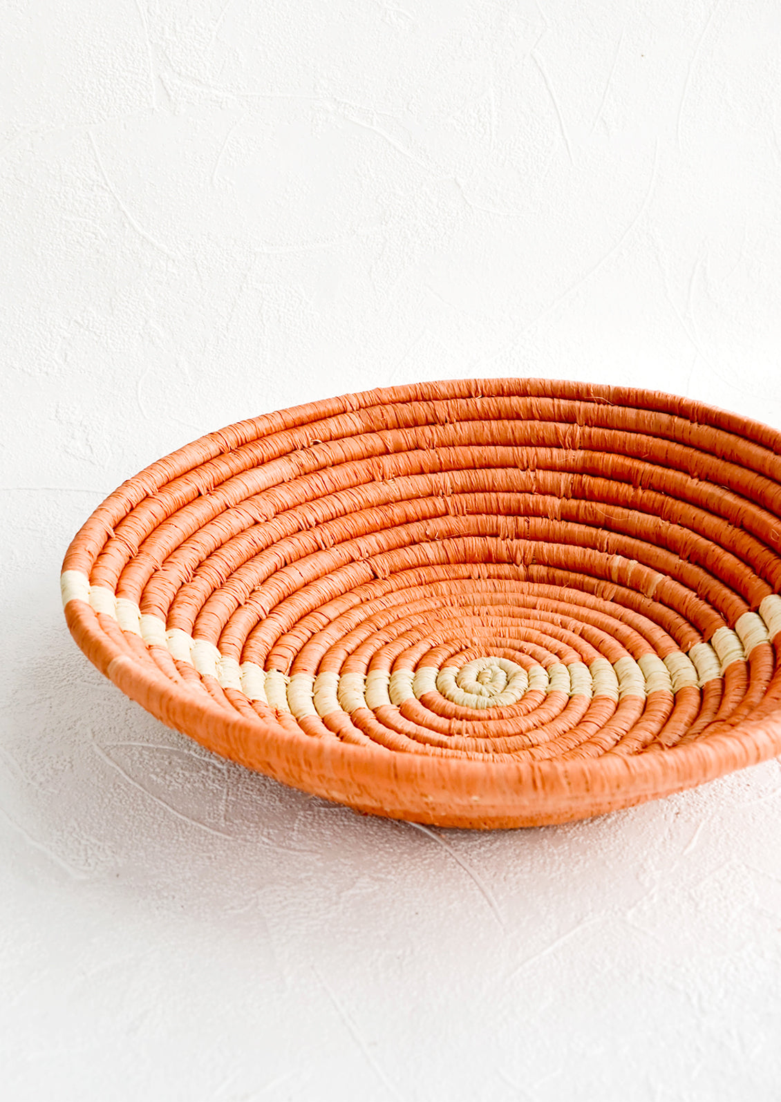 Shallow, peach colored woven raffia bowl with natural streak across middle